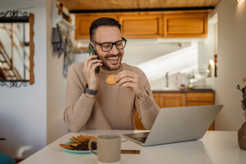 Adult caucasian man eat breakfast talk on mobile phone work from home