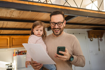 Adult man hold his two years old daughter and talk on mobile phone