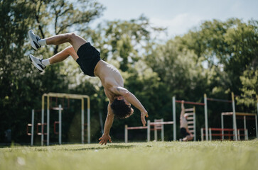 A man performing an impressive back flip in an outdoor park, highlighting athletic skills, fitness,...