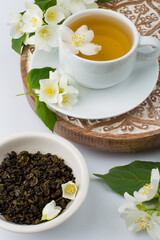 Cup with green tea and jasmine flowers on a stand on a white background.