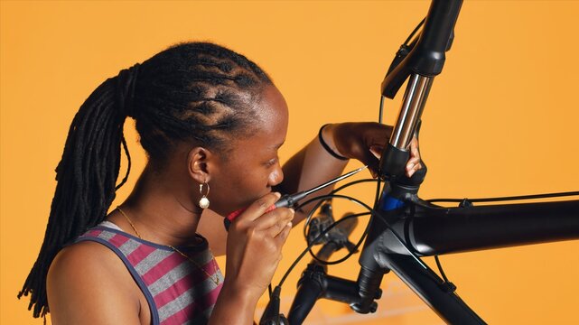 BIPOC technician uses screwdriver to unmount bicycle handlebars, testing components quality in studio background atelier shop. Specialist mechanic unscrewing bike parts in order to mend them, camera A - Powered by Adobe