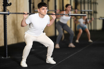 Young man in sportswear training with barbell in gym