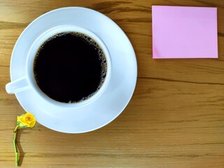 A cup of coffee, note pad and yellow rosebud on wooden table. Top view
