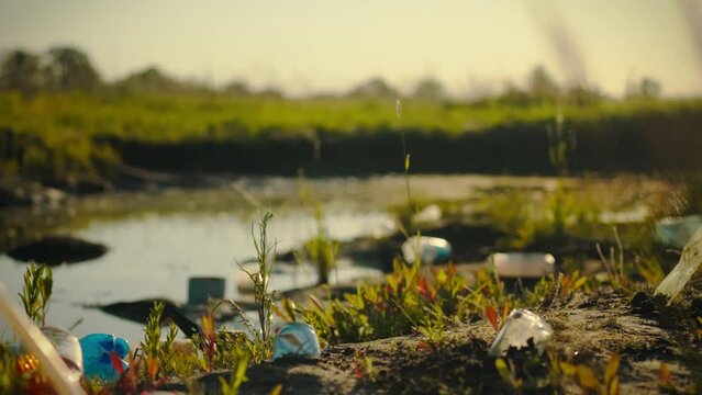 A slow moving camera shows pollution in the green area. Plastic trash is scattered along the coastal area. The background of the park is polluted with single-use plastic. Idea Save our land