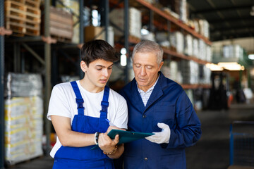 Guy manager conducts survey of elderly man employee of wholesale warehouse of construction goods...