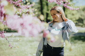 Carefree young lady in casual clothes smiles during a leisurely stroll in an urban park on a sunny...