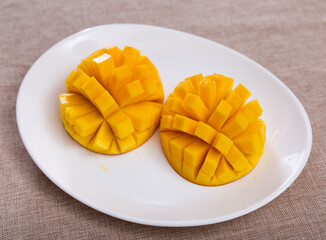 Two halves of ripe yellow mango cut into cubes lie on white round plate.Isolated