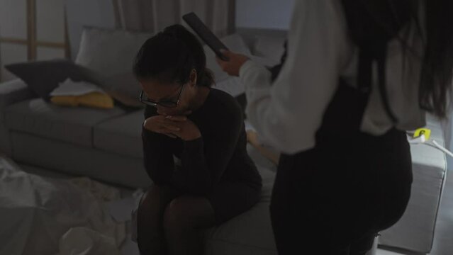 Distressed woman interrogated by policewoman in a dimly lit room, reflecting a tense investigation scenario.