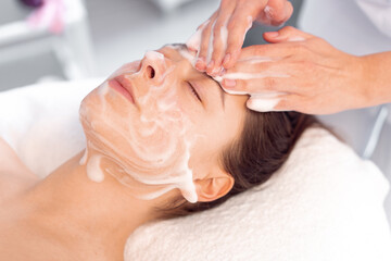 Cosmetologist cleanses the skin with foam. Woman's skin care procedure in beauty clinic. Natural...