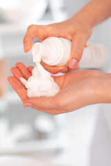 Esthetician hands holding white bottle with peeling or cleansing foam. Experienced beautician preparing to apply cleansing foam in beauty clinic. Moisturizing Face Skin, Facial Massage.