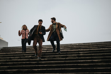 Three business professionals engaging in a discussion while walking down the outdoor stairs,...