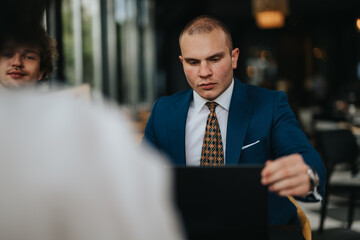Professional businessman in a blue suit intently working on his laptop in a modern coffee bar setting. Capturing the essence of focus and productivity.