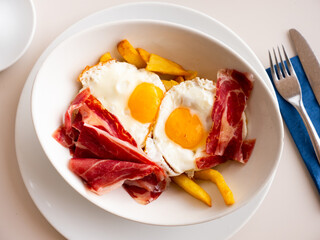 Plate of appetizing hearty breakfast of fried eggs with slices of delicious bacon and French fries