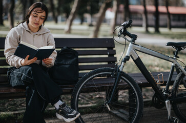 A serene setting where a female enjoys reading a book outdoors, with her bike and backpack nearby,...