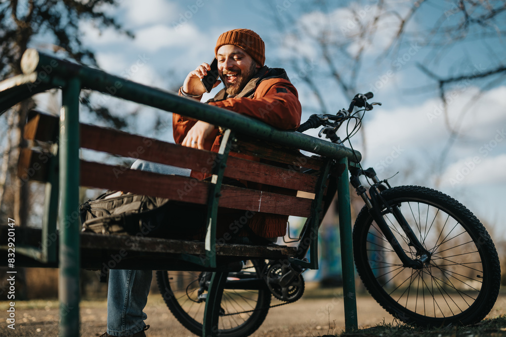 Wall mural A young man in casual attire enjoying a quiet moment on a park bench beside his mountain bike, embracing the tranquility of nature.