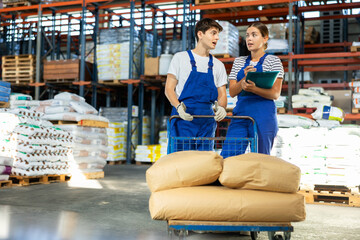 Young woman and young guy warehouse workers in overalls discussing documents