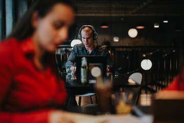 Young business entrepreneurs working together in a modern office space. Focused man with headphones and laptop in background, woman in foreground.