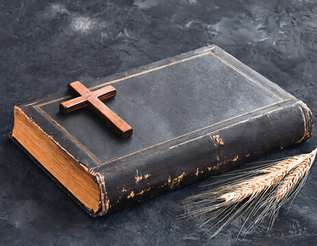 Old holy bible with a wooden cross and spikelets of wheat on a dark background
