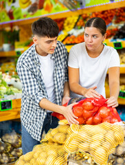 Positive couple choosing fresh foods in fruit and vegetable section of supermarket