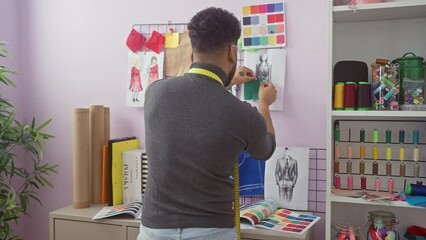 African-american tailor organizing sketches in a colorful atelier, surrounded by threads and fabrics. - Powered by Adobe