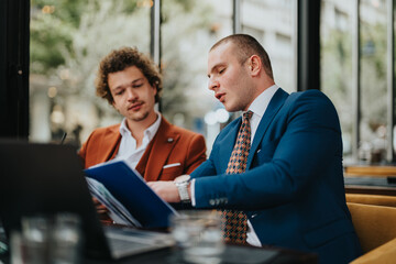 Two businessmen in formal attire engaged in a discussion over work documents in a modern coffee bar setting.