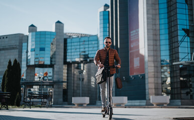 Confident businessman commuting on an electric scooter with a stylish outfit and carrying a leather bag in an urban setting.