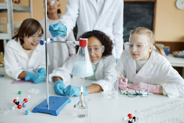 Group of ethnically diverse middle school students wearing lab coats and goggles watching chemical reaction during experiment in class