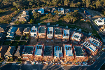 Late afternoon aerial view of modern houses with solar panels and scaffolding under construction in the outer suburbs of Sydney, Australia.