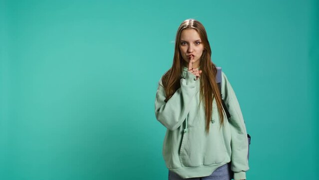 Stern woman doing shushing hand gesturing, irritated by noise, having negative mood. Girl placing finger on lips, doing quiet sign gesture, isolated over studio background, camera B