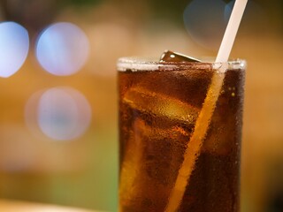 Cola with ice cubes on a dark lights bokeh background, close-up