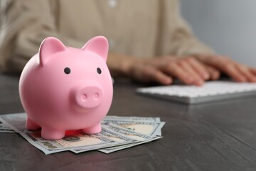 Woman at black table, focus on pink piggy bank and banknotes. Space for text