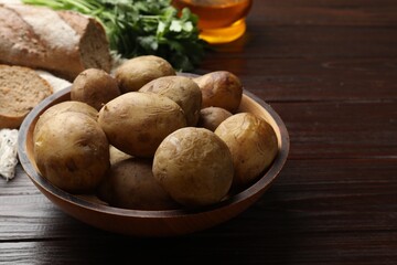 Boiled young potatoes in bowl, bread and parsley on wooden table