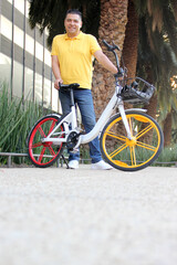 Dark-skinned Latino adult man uses a public bicycle that he pays for through an app on his cell...