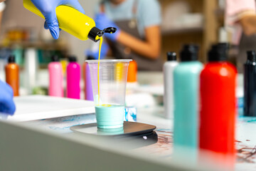 Group of Asian generation z people learning acrylic pouring art on canvas workshop at art studio. Young artist university student enjoy and fun creating colorful abstract modern art painting in class.