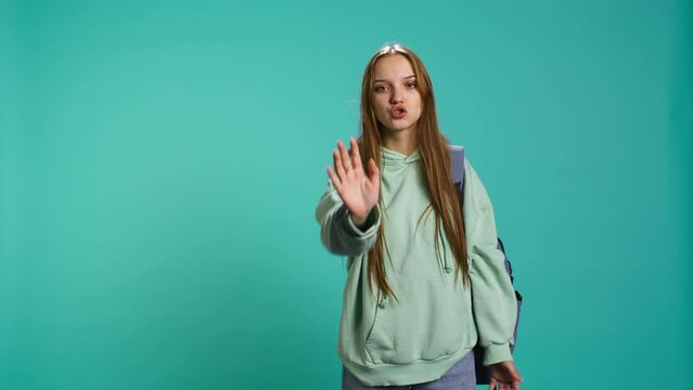 Assertive young woman doing stop hand gesture and talking. Annoyed girl doing firm halt sign gesturing, wishing to end concept, isolated over blue studio background, camera B