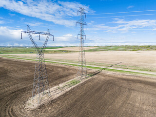 Electrical transmission towers pair aerial shot overlooking agriculture fields and country road in...