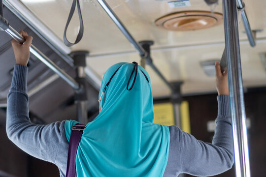 A standing woman in traditional Islamic dress holds with both hands while bus ride - Powered by Adobe