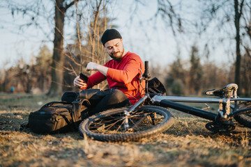A young man listening to music on headphones and dancing while taking a break next to his bicycle...