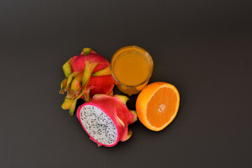 A glass of freshly squeezed fruit juice on a black background, next to half a ripe pitaya and an...