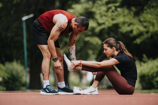 Caring male runner helps his partner deal with a leg injury on a running track, showcasing concern and support in a natural setting.