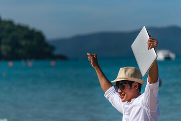 Man traveler use laptop on summer beach blue sky. Asian man wear casual short pants tropical shirt...