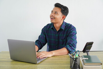 pensive young asian man in blue shirt sit work at wooden desk with pc laptop isolated on white...