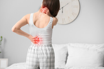 Young woman suffering from back pain in bedroom