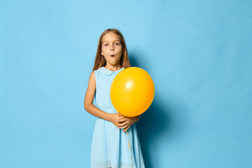Little girl in a colorful dress joyfully holding a yellow balloon against a vibrant blue background