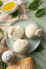 Plate of tasty Burrata cheese with basil and oil on green wooden background