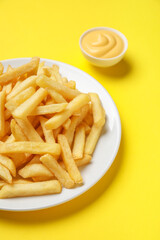 Plate with golden french fries and cheese sauce on yellow background, closeup