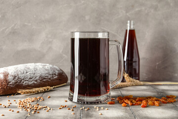 Mug of tasty kvass, bread, raisins and wheat grains on table