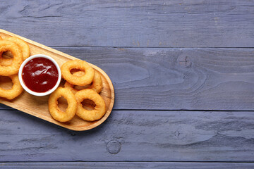 Board with fried breaded onion rings and ketchup on blue wooden background
