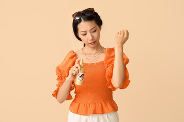 Young Asian woman with mosquito repellent on beige background