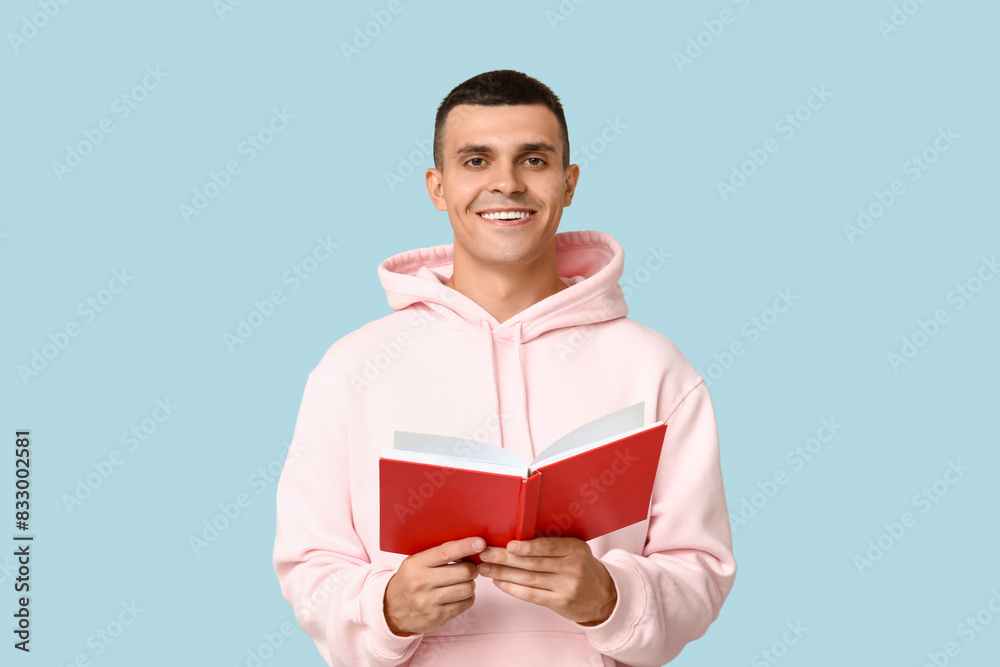 Poster Handsome young man reading book on blue background